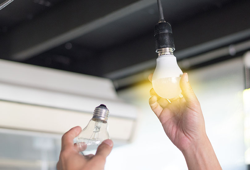 Power saving concept. Asia man changing compact-fluorescent (CFL) bulbs with new LED light bulb.