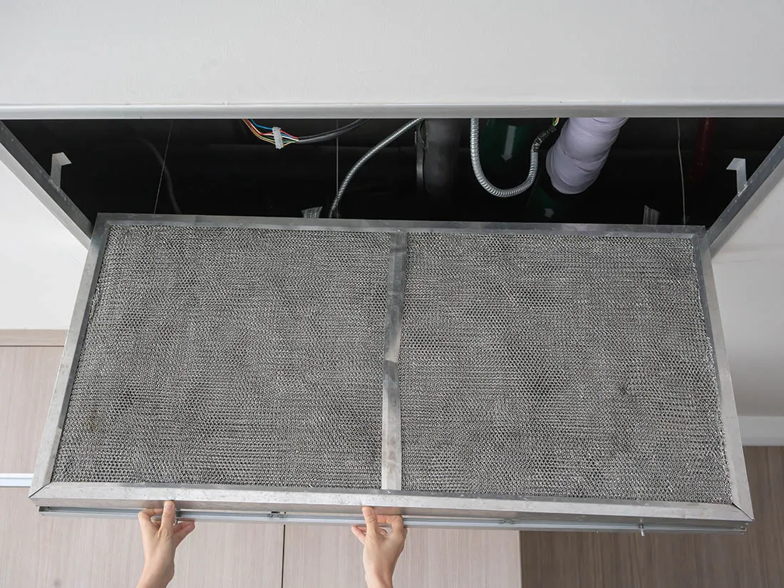 Hand reaching up to open filter holder for air conditioning filter