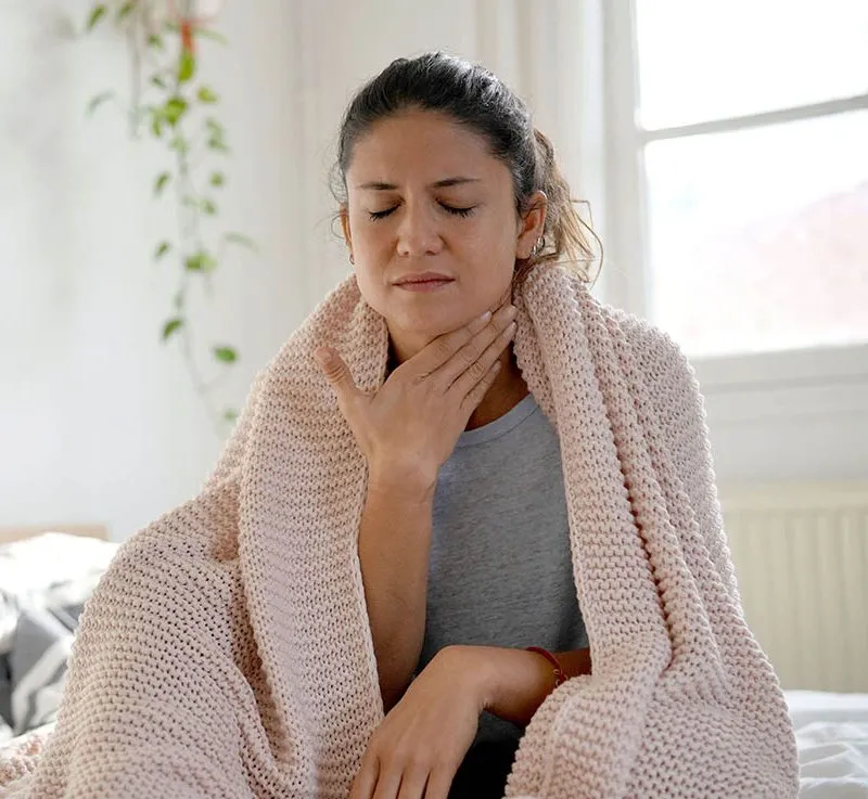 Sick woman sitting in bed with a blanket wrapped around her